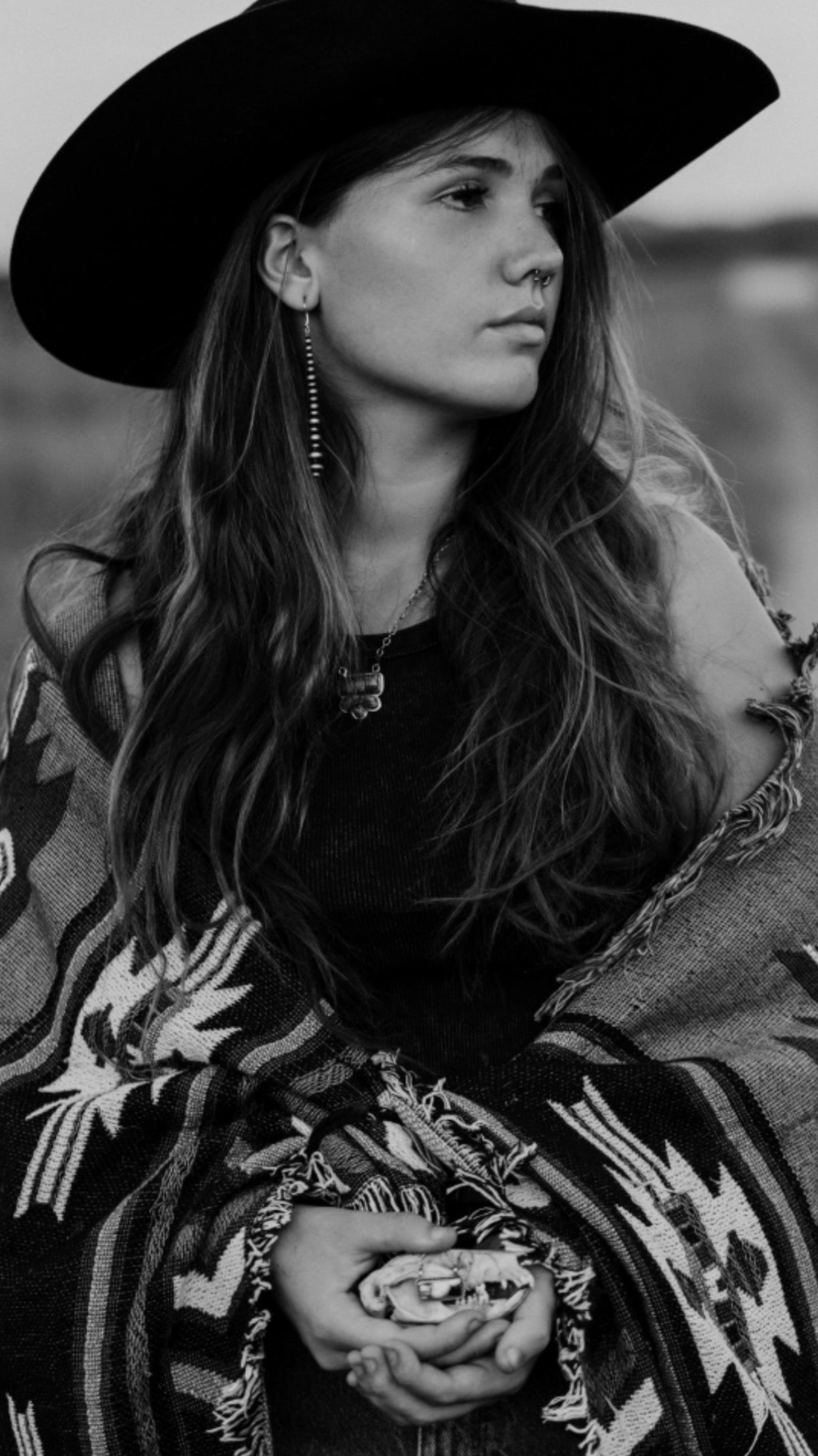 Black and white photo of a person wearing a wide-brimmed hat and patterned garment.